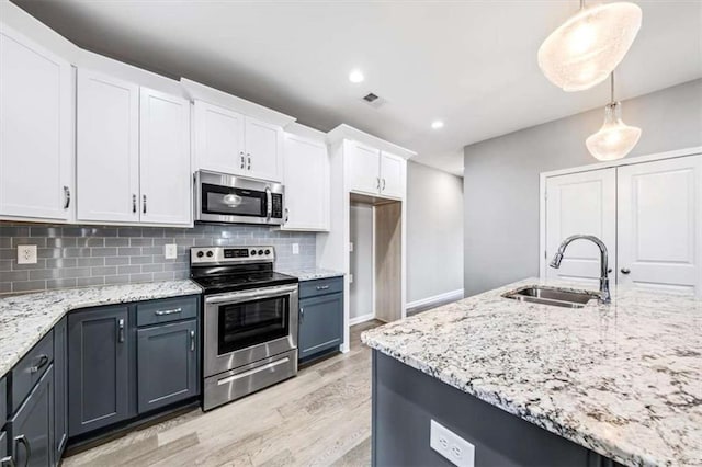 kitchen with light stone counters, stainless steel appliances, tasteful backsplash, white cabinetry, and a sink