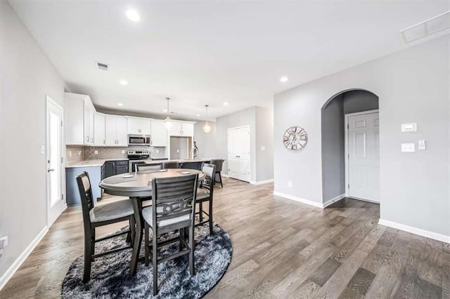 dining space with arched walkways, visible vents, baseboards, and wood finished floors