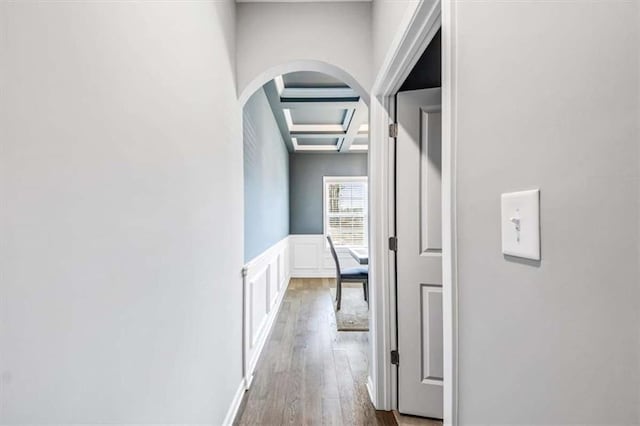 corridor with arched walkways, coffered ceiling, wainscoting, wood finished floors, and a decorative wall