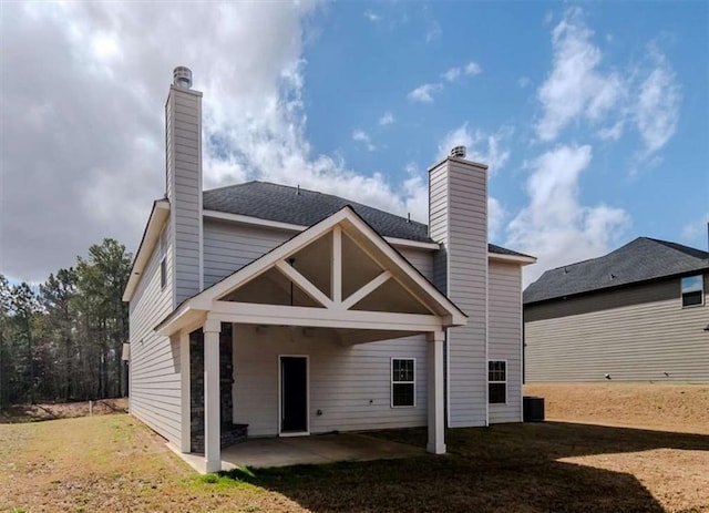 rear view of property featuring a patio area, a lawn, and a chimney