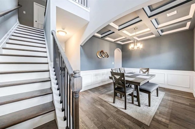 dining space featuring arched walkways, a notable chandelier, coffered ceiling, beam ceiling, and dark wood finished floors