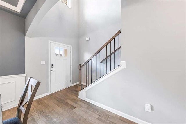 entrance foyer with arched walkways, a wainscoted wall, wood finished floors, baseboards, and stairs