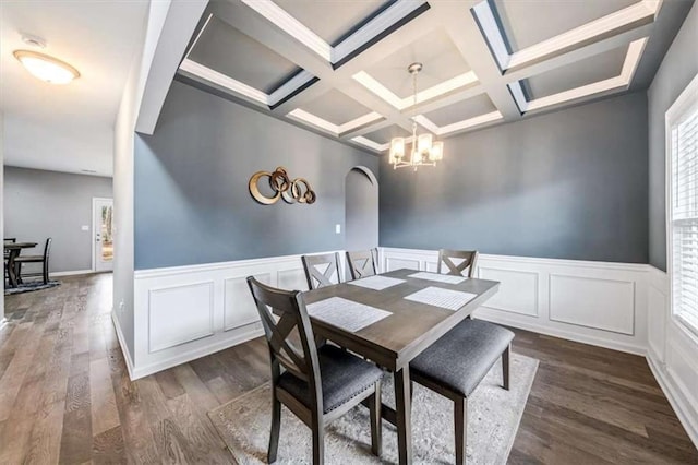 dining space featuring arched walkways, dark wood-style flooring, coffered ceiling, wainscoting, and an inviting chandelier