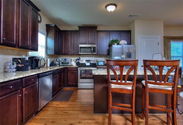 kitchen featuring light stone countertops, appliances with stainless steel finishes, backsplash, sink, and light hardwood / wood-style flooring