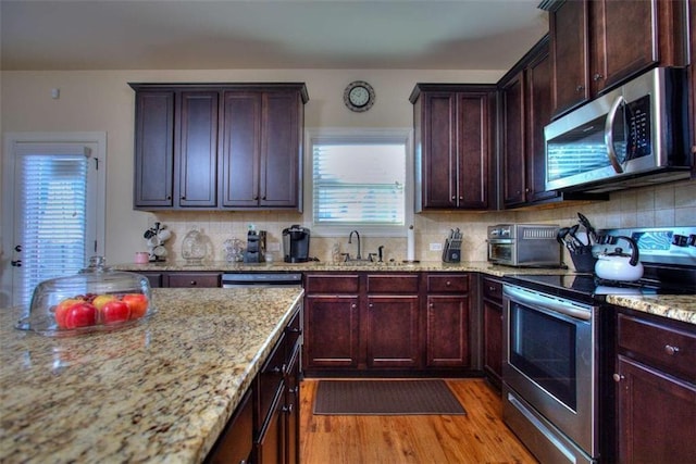 kitchen with sink, light stone counters, decorative backsplash, appliances with stainless steel finishes, and light wood-type flooring