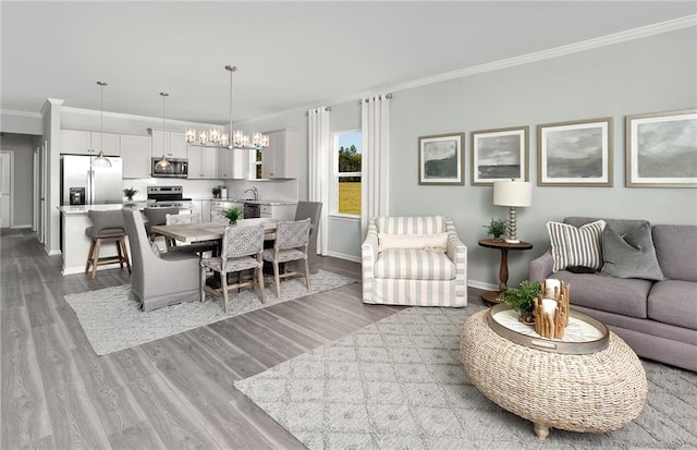 living room featuring a chandelier, light hardwood / wood-style floors, sink, and crown molding