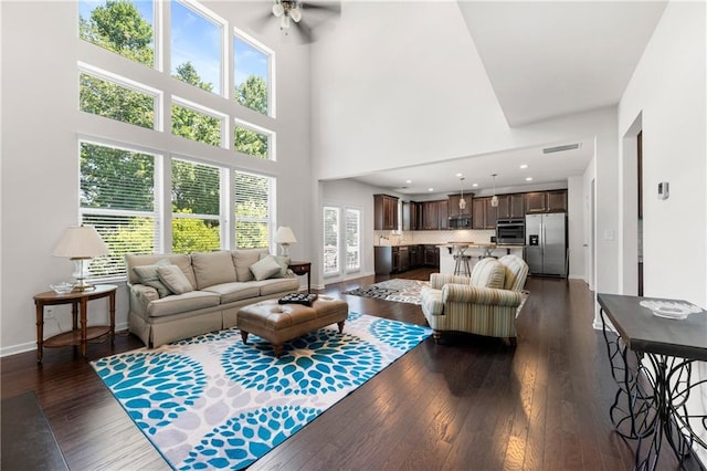 living area featuring a ceiling fan, a high ceiling, dark wood-style floors, and baseboards