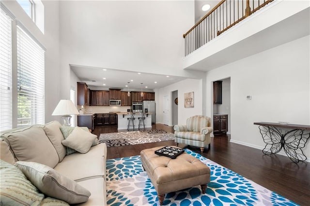 living area with dark wood-style flooring, a high ceiling, a healthy amount of sunlight, and baseboards