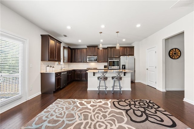 kitchen with dark brown cabinetry, a kitchen island, visible vents, appliances with stainless steel finishes, and tasteful backsplash