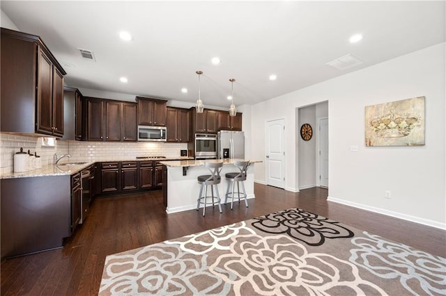 kitchen featuring dark brown cabinetry, a kitchen island, a kitchen bar, dark wood finished floors, and stainless steel appliances