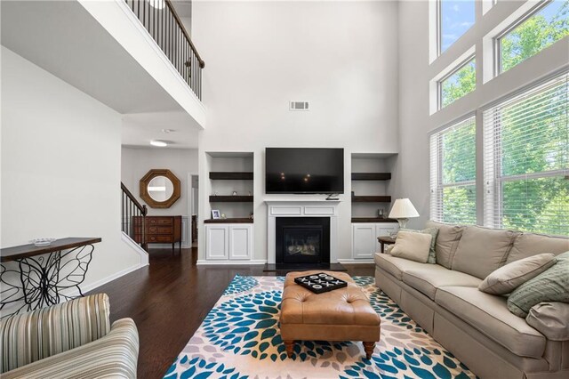 living area with visible vents, stairs, a towering ceiling, dark wood-type flooring, and built in shelves