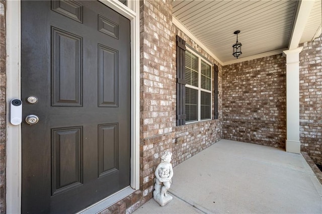 doorway to property featuring a porch and brick siding
