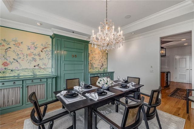 dining room with crown molding, light wood finished floors, a chandelier, and a tray ceiling