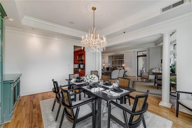 dining room with visible vents, decorative columns, a chandelier, a tray ceiling, and light wood finished floors