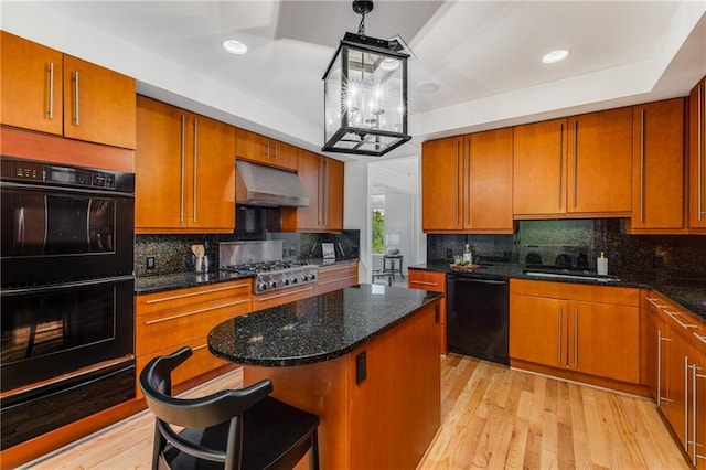 kitchen featuring brown cabinetry, a sink, under cabinet range hood, and black appliances