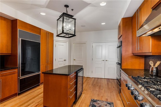 kitchen featuring stainless steel gas cooktop, under cabinet range hood, built in fridge, brown cabinets, and light wood finished floors