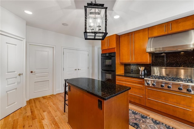 kitchen with light wood-style floors, dobule oven black, brown cabinetry, tasteful backsplash, and under cabinet range hood