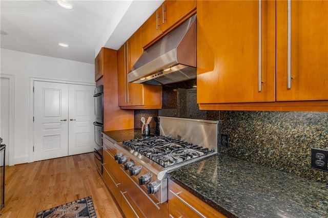 kitchen with brown cabinets, light wood-style flooring, stainless steel gas stovetop, tasteful backsplash, and under cabinet range hood