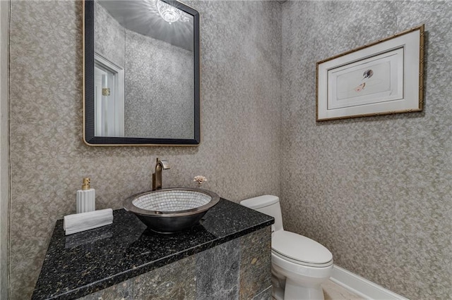 half bath with toilet, wallpapered walls, and vanity