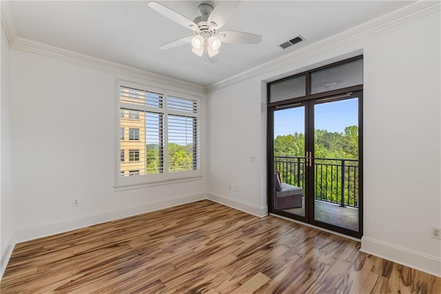 empty room featuring a ceiling fan, visible vents, crown molding, wood finished floors, and baseboards