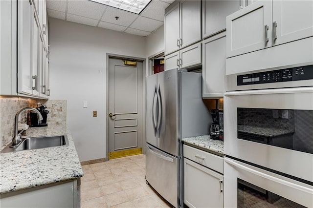 kitchen featuring baseboards, a paneled ceiling, a sink, backsplash, and stainless steel appliances