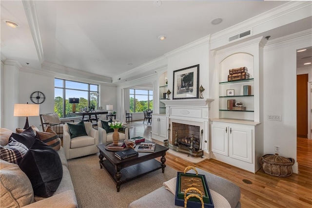 living room with crown molding, visible vents, a fireplace, and light wood-type flooring