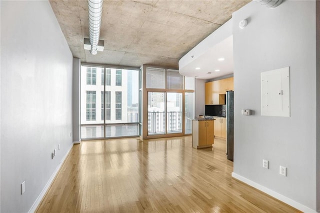 unfurnished living room featuring baseboards, a wall of windows, light wood finished floors, and electric panel