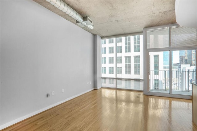spare room with baseboards, a wall of windows, and wood finished floors