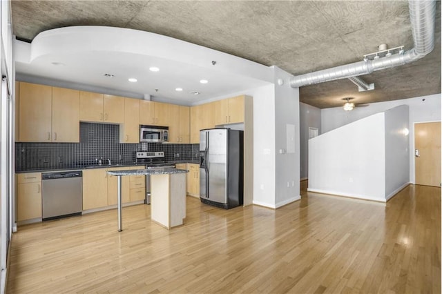 kitchen with light brown cabinetry, appliances with stainless steel finishes, light wood-style flooring, open floor plan, and backsplash