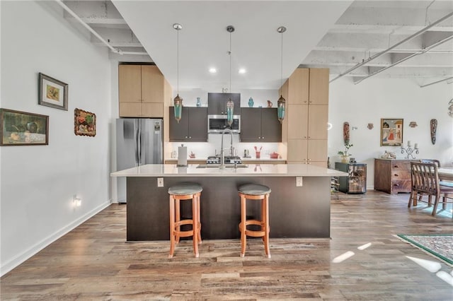 kitchen featuring pendant lighting, hardwood / wood-style floors, a kitchen island with sink, appliances with stainless steel finishes, and a breakfast bar area