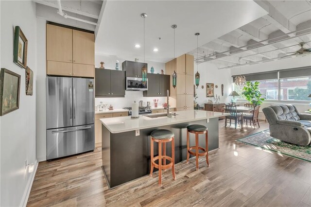 kitchen featuring sink, stainless steel appliances, pendant lighting, a kitchen bar, and a center island with sink