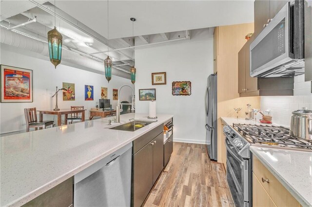 kitchen with sink, light stone counters, light hardwood / wood-style flooring, pendant lighting, and appliances with stainless steel finishes