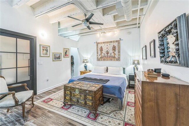 bedroom featuring a towering ceiling, hardwood / wood-style flooring, track lighting, and ceiling fan