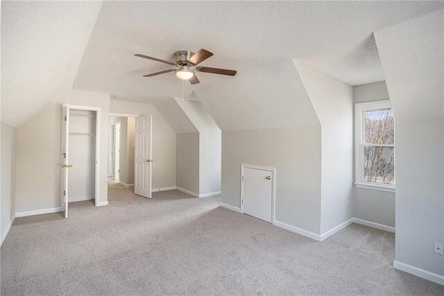 additional living space with light carpet, a textured ceiling, vaulted ceiling, and ceiling fan