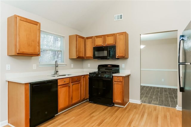 kitchen with light hardwood / wood-style floors, sink, black appliances, and vaulted ceiling