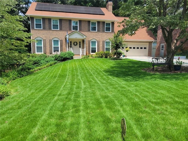 colonial inspired home with solar panels, a front lawn, and a garage