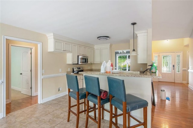 208 Stonington Dr, Mount Airy, GA 30563 - kitchen featuring appliances with stainless steel finishes, a breakfast bar, pendant lighting, baseboards, and light wood finished floors