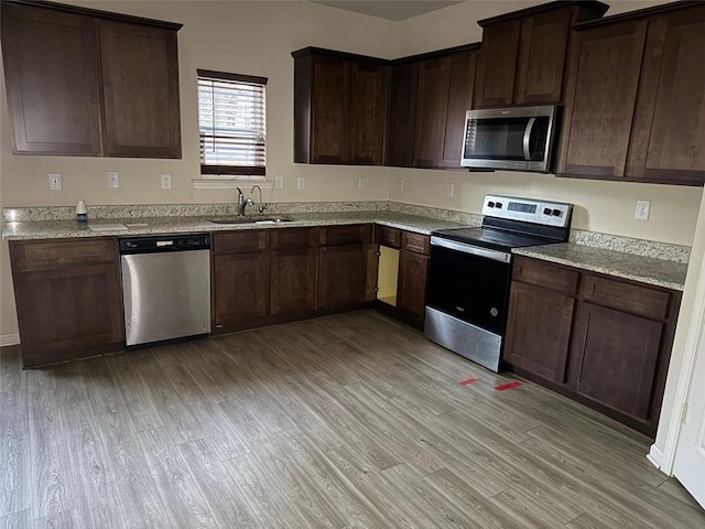 kitchen featuring light hardwood / wood-style floors, light stone countertops, appliances with stainless steel finishes, sink, and dark brown cabinetry