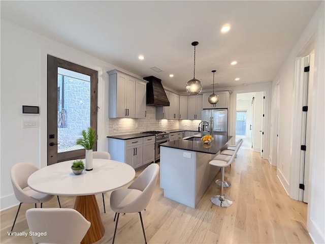 kitchen with premium range hood, a kitchen island with sink, a sink, appliances with stainless steel finishes, and dark countertops