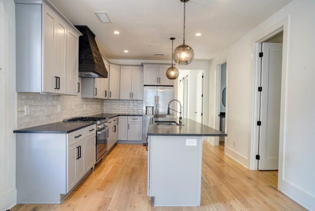 kitchen with dark countertops, light wood finished floors, custom range hood, appliances with stainless steel finishes, and a sink