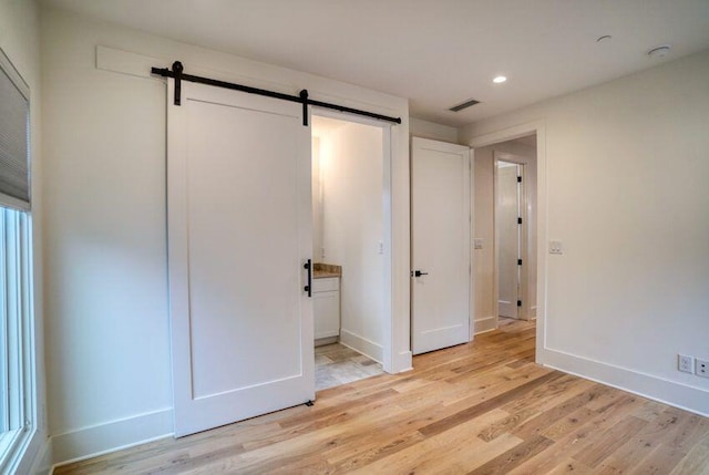 unfurnished bedroom featuring light wood-type flooring, a barn door, baseboards, and visible vents