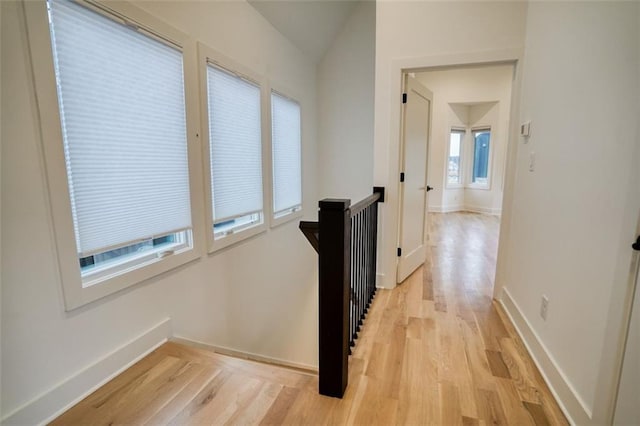 hall with lofted ceiling, light wood-style flooring, an upstairs landing, and baseboards