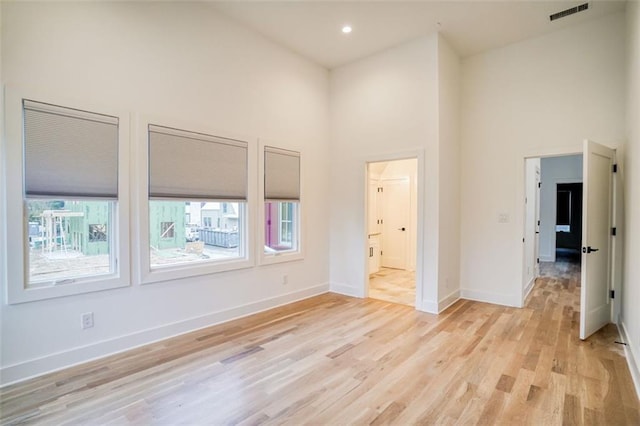 unfurnished room with baseboards, visible vents, light wood finished floors, a high ceiling, and recessed lighting