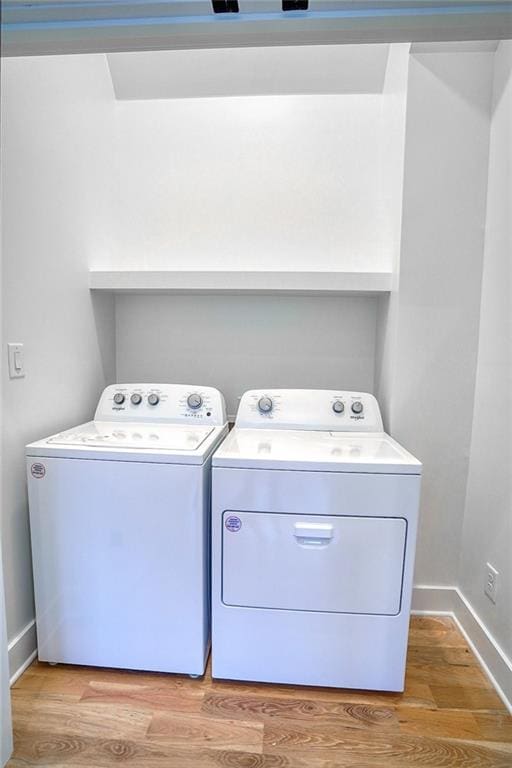 clothes washing area featuring light wood-type flooring, baseboards, laundry area, and washer and clothes dryer