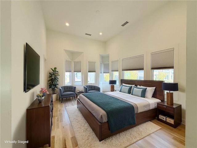 bedroom featuring visible vents, light wood-style flooring, a high ceiling, and multiple windows