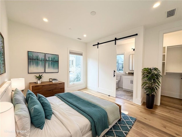 bedroom with recessed lighting, visible vents, light wood-style flooring, and a barn door