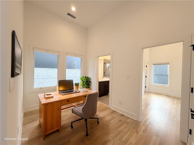 home office with visible vents, baseboards, light wood-type flooring, and a towering ceiling