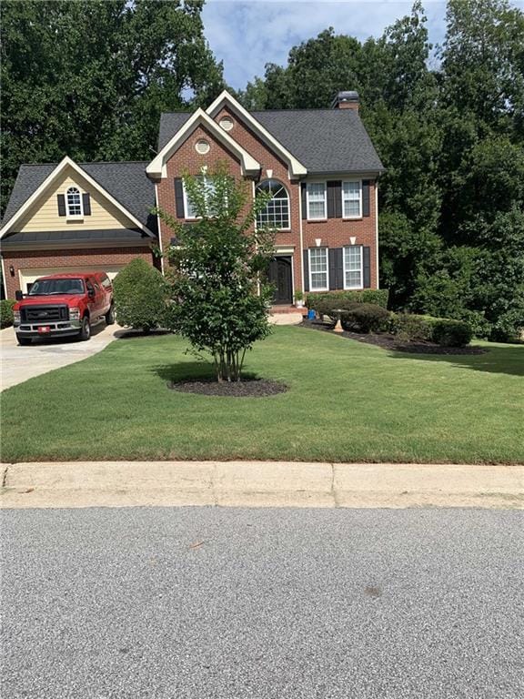 colonial-style house with concrete driveway, brick siding, an attached garage, and a front lawn