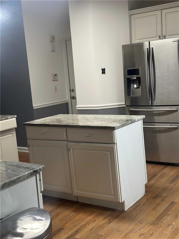 kitchen featuring light stone counters, white cabinets, a kitchen island, wood finished floors, and stainless steel fridge with ice dispenser