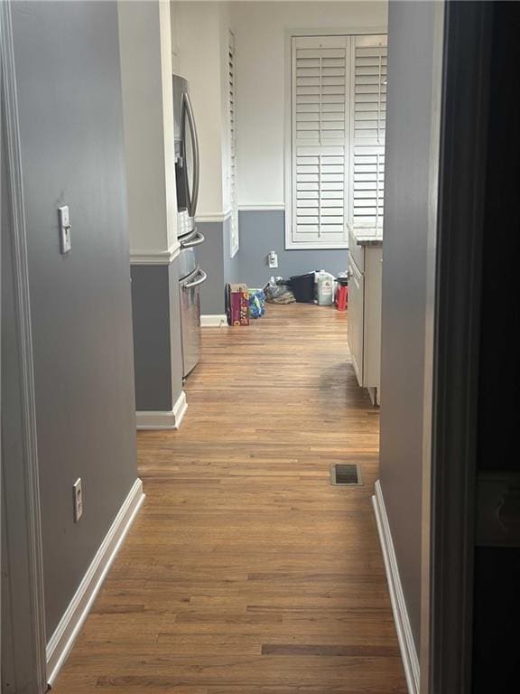 hall featuring baseboards, visible vents, and wood finished floors